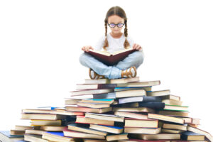 Menina sentada em pilha de livros ilustra os livros infantis por faixa etária.